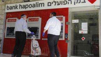 إسرائيليون بجوار ماكينة صرف آلي لبنك هبوعليم في القدس المحتلة، 1 مايو 2020 (فرانس برس)