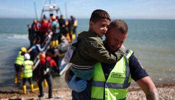 شرطي بريطاني يحمل طفلاً خلال انتشال لاجئين من قارب صغير، 16 أغسطس 2023 (فرانس برس)