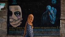 امرأة أفغانية وجدارية حول حقوق المرأة والطفل في أفغانستان (نافا جامشيد/ Getty)