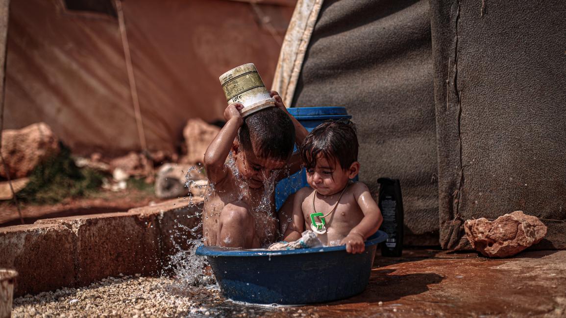 طفلان سوريان يلعبان بالمياه في أحد مخيمات إدلب (الأناضول)