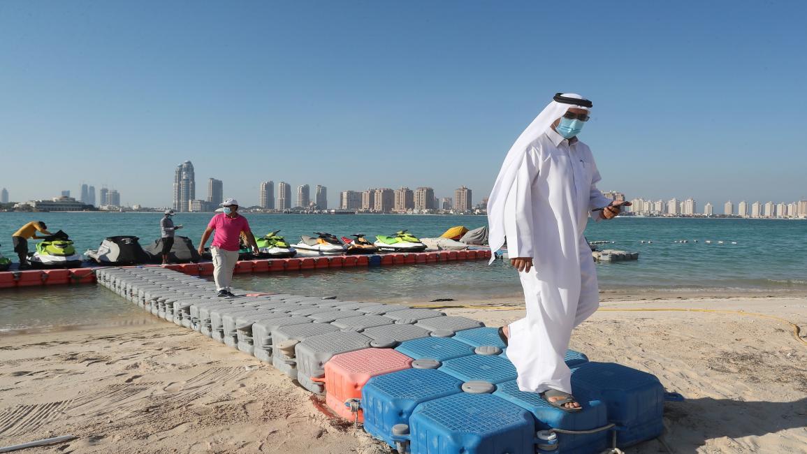 QATAR-HEALTH-VIRUS Men, wearing protective masks, walk on a plastic pier at Katara beach in the Qatari capital Doha on July 1, 2020 as the country moves into the second phase of its four-step plan to lift COVID-19 lockdown. - People in Qatar cautiously returned to beaches as the Gulf nation, which has one of the world's highest total per capita coronavirus infection rates, continued to reopen society. Sun-lovers and jetski enthusiasts braved temperatures of 39 degrees celsius (102 Fahrenheit) at Doha's Kata