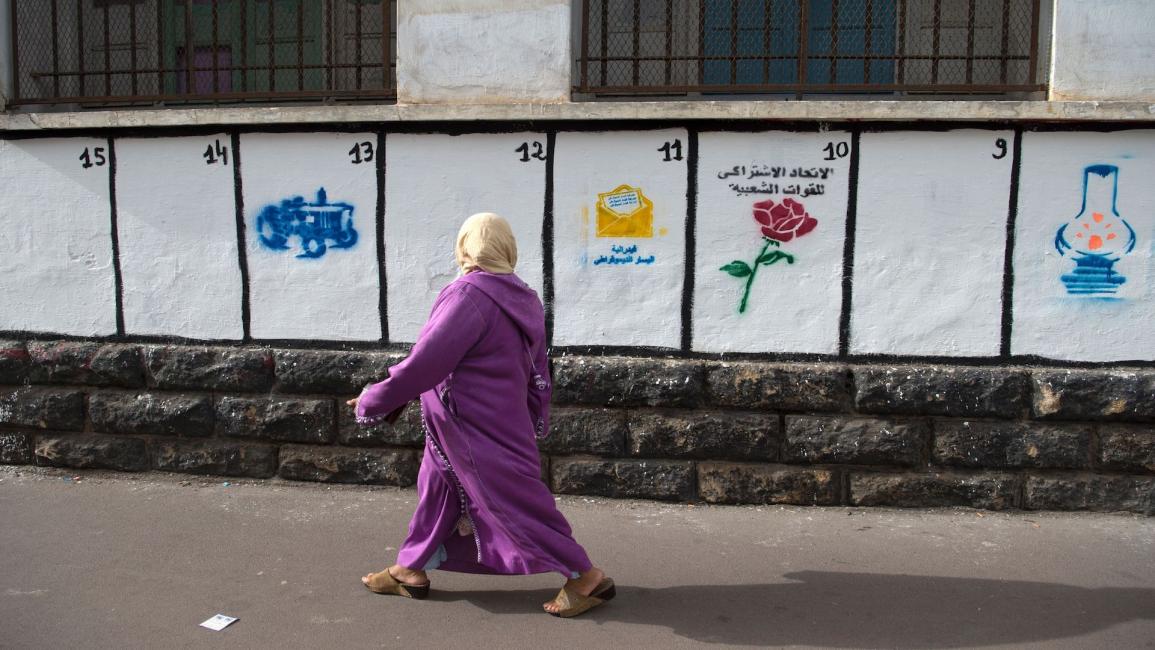 مرأة مغربية تمر عبر جدار رسمت عليه رموز الأحزاب السياسية المتنافسة في الانتخابات البرلمانية بالعاصمة المغربية الرباط في 7 أكتوبر 2016