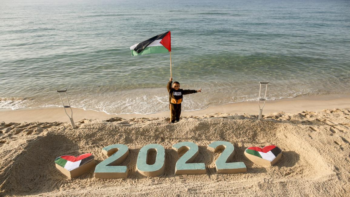 طفل فلسطيني يعمل علم فلسطين على شاطئ غزة في 28/ 12/ 2021 (Getty)