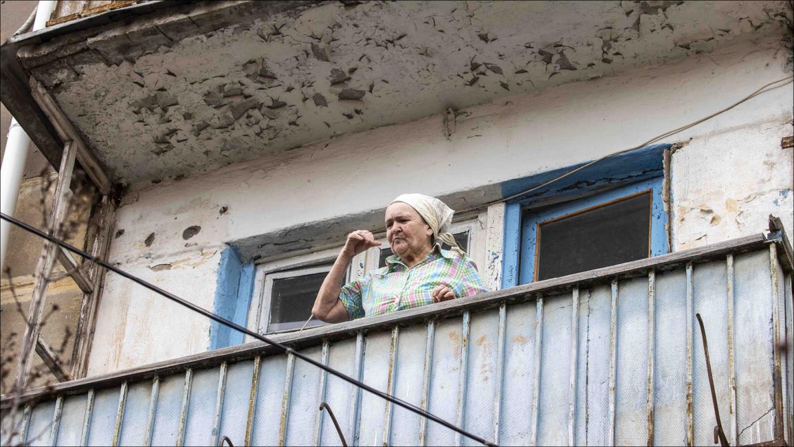 امرأة تترقب حركة الشارع من على شرفة منزلها في بلدة شاستيا في لوهانسك (ايتاك شنال/الأناضول)