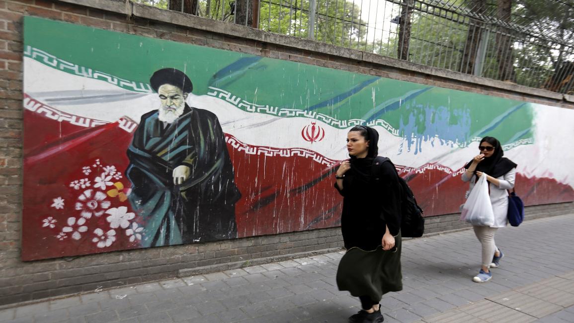 شابتان إيرانيتان أمام جدارية تحمل رسم الخميني- فرانس برس