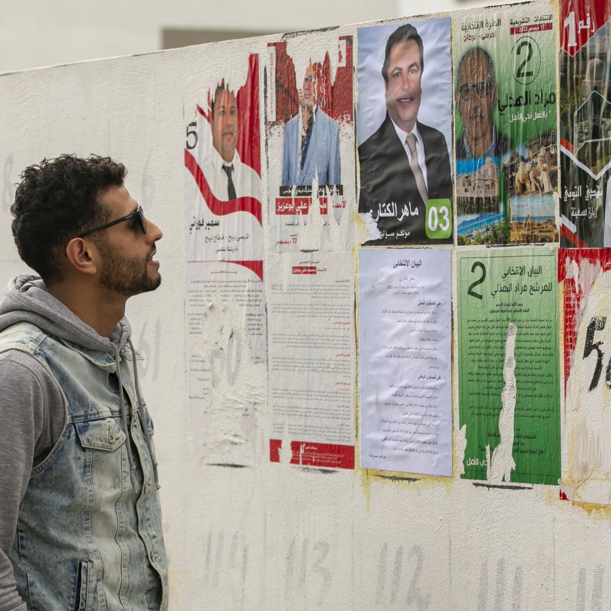 مواطن تونسي ينظر إلى ملصقات انتخابية في العاصمة تونس، 12 ديسمبر (ياسين القايدي/الأناضول)