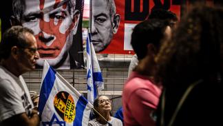 متظاهرة تجلس تحت صور نتنياهو في تل أبيب