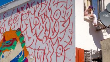 امرأة تطلّ من نافذة مجاورة لجدارية للفنان عمر الحمزي في الرباط