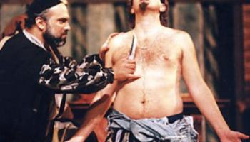 مشهد من مسرحية تاجر البندقية - شايلوك يهم باقتطاع رطل من لحم انطونيو (مواقع التواصل)