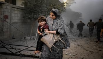 فلسطينية تهرب مع ابنها بين أنقاض المباني بعد قصف إسرائيلي في دير البلح وسط قطاع غزّة في 6/11/ 2023 (الأناضول)