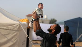 أب فلسطيني يحمل ابنه الرضيع في دير البلح، 27 كانون الأوّل/ ديسمبر 2023 (Getty)