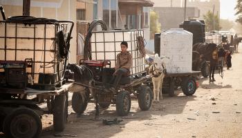 صبي يجلس على عربة يجرها حمار محمّلة بخزان مياه وسط انقطاع الإمدادات (محمود الهمس/Getty)