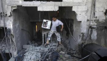 رجل فلسطيني يزيل حاسبه من بين أنقاض منزله الذي دمّره الاحتلال الإٍسرائيلي في غزّة، أيار/ مايو 2014 (Getty)