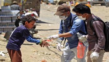 متطوعان يمنيان يعقمان يدي أحد الأطفال في صنعاء (Getty)