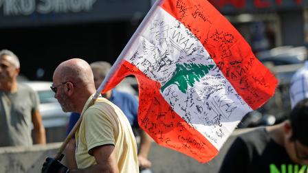 متظاهر يرفع علم لبنان يحمل توقيعات المحتجين على الفساد (فرانس برس)