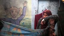 امرأةٌ تستند إلى عمود خيمة نُصبت في مدرسة حوّلها العُدوان إلى ملجأ، ديرالبلح، 24 شباط/ فبراير 2024 (Getty)